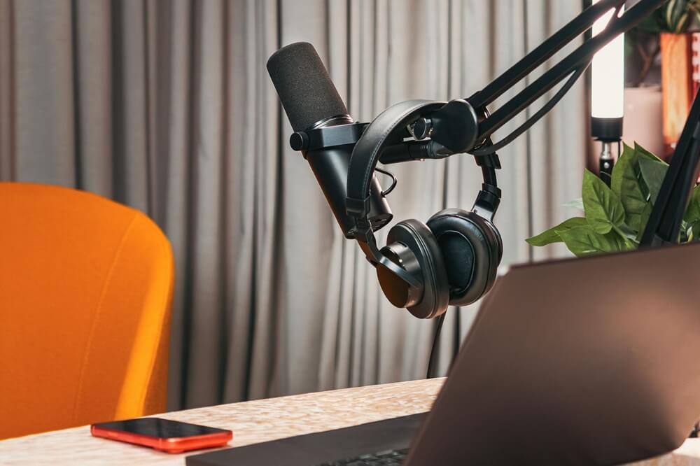 Image of a microphone and some headphones above a laptop. An orange chair is to the left